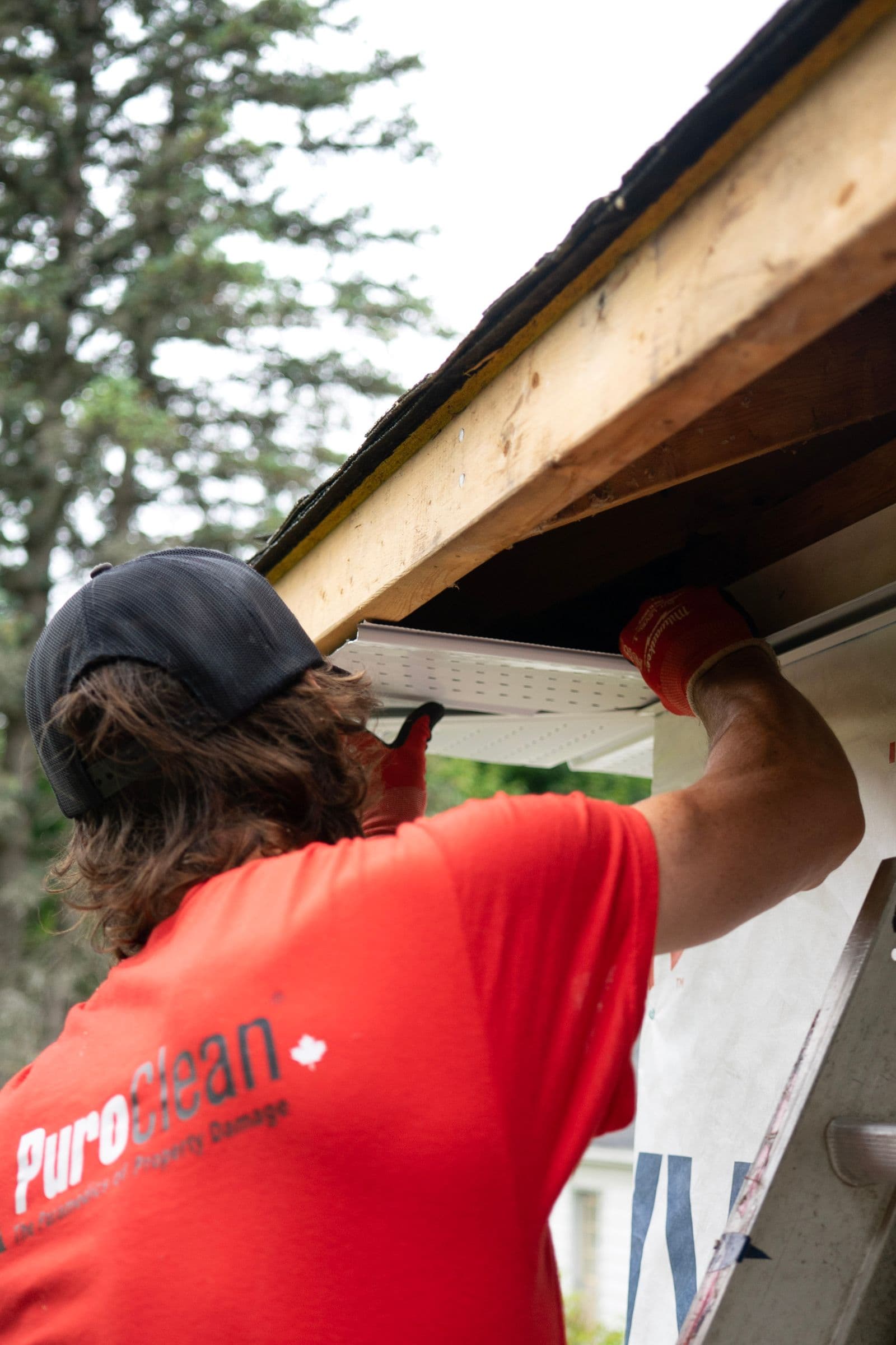 Worker clearing debris from residential gutters and checking downpipes